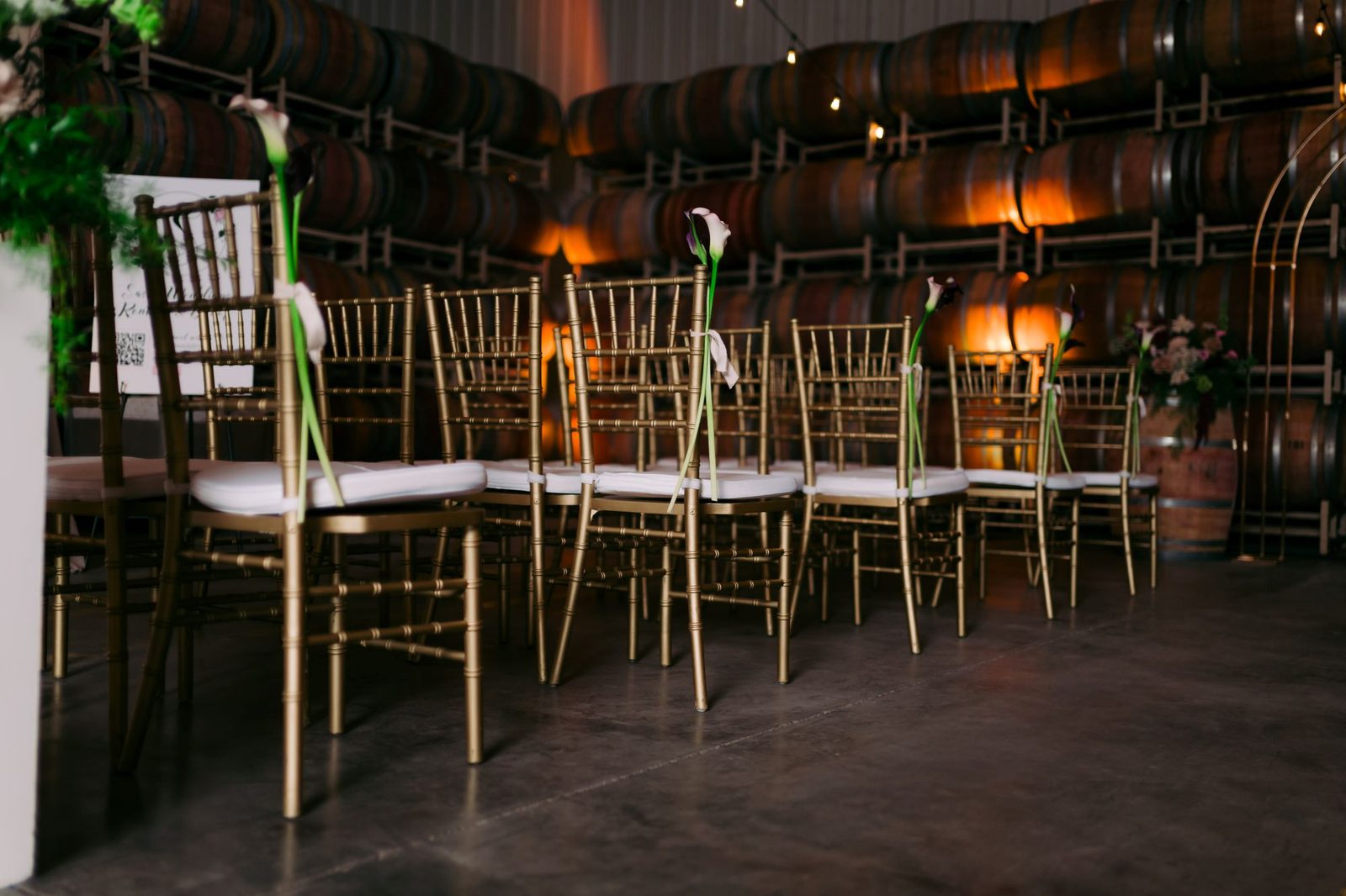 Gold chiavari chairs accented with calla lilies arranged for a ceremony among the wine barrels at The Barrel Hall