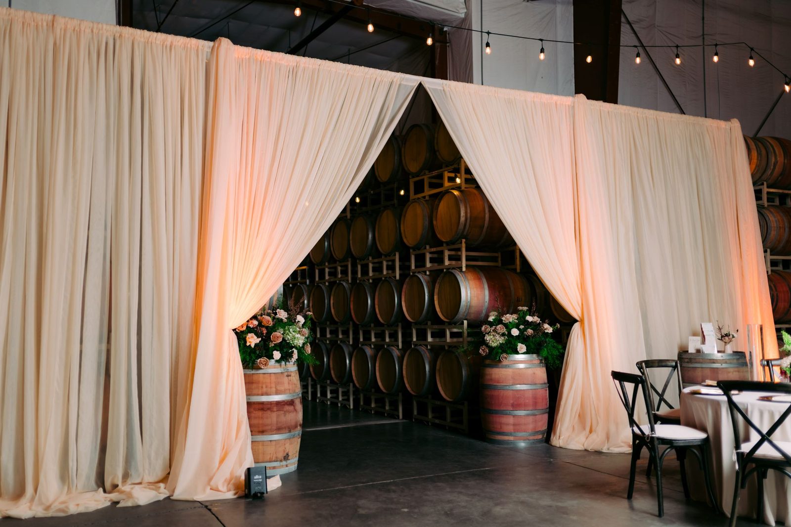 Draped entrance flanked by floral-topped wine barrels at The Barrel Hall at Goose Ridge Estate
