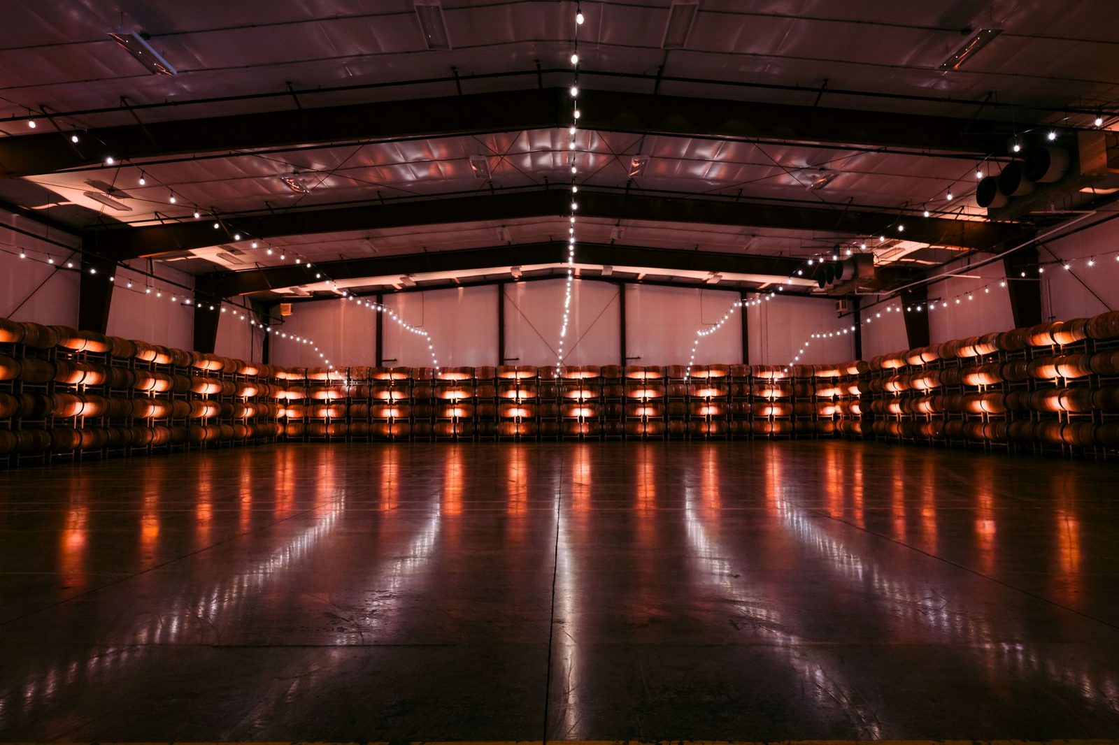 The Barrel Hall event space at Goose Ridge Estate, an open floor framed by walls of stacked wine barrels and warm string lights