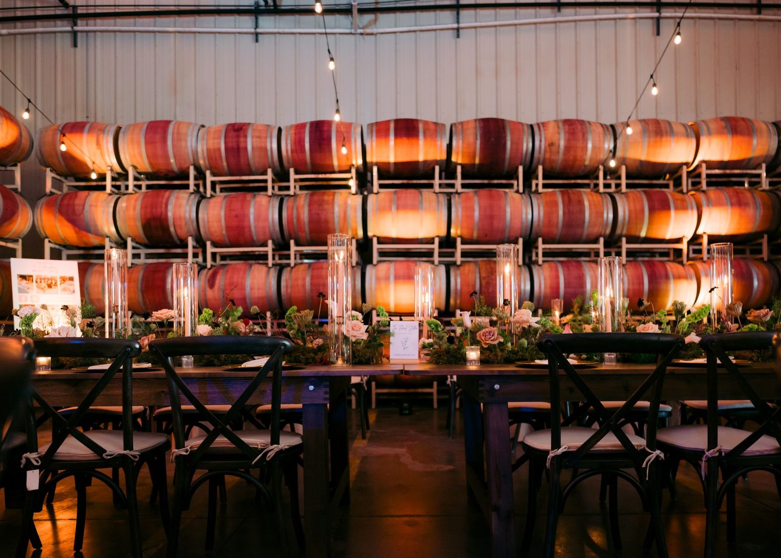 Long banquet table set with candles and a floral runner in front of a wall of wine barrels at The Barrel Hall