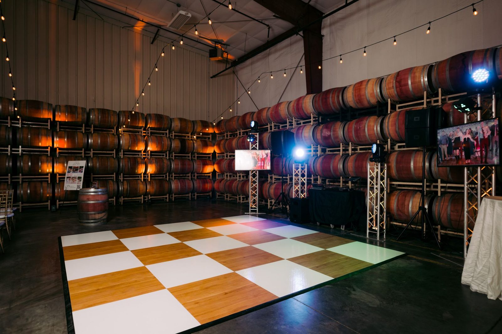 Checkered dance floor with DJ lighting set against walls of wine barrels at The Barrel Hall