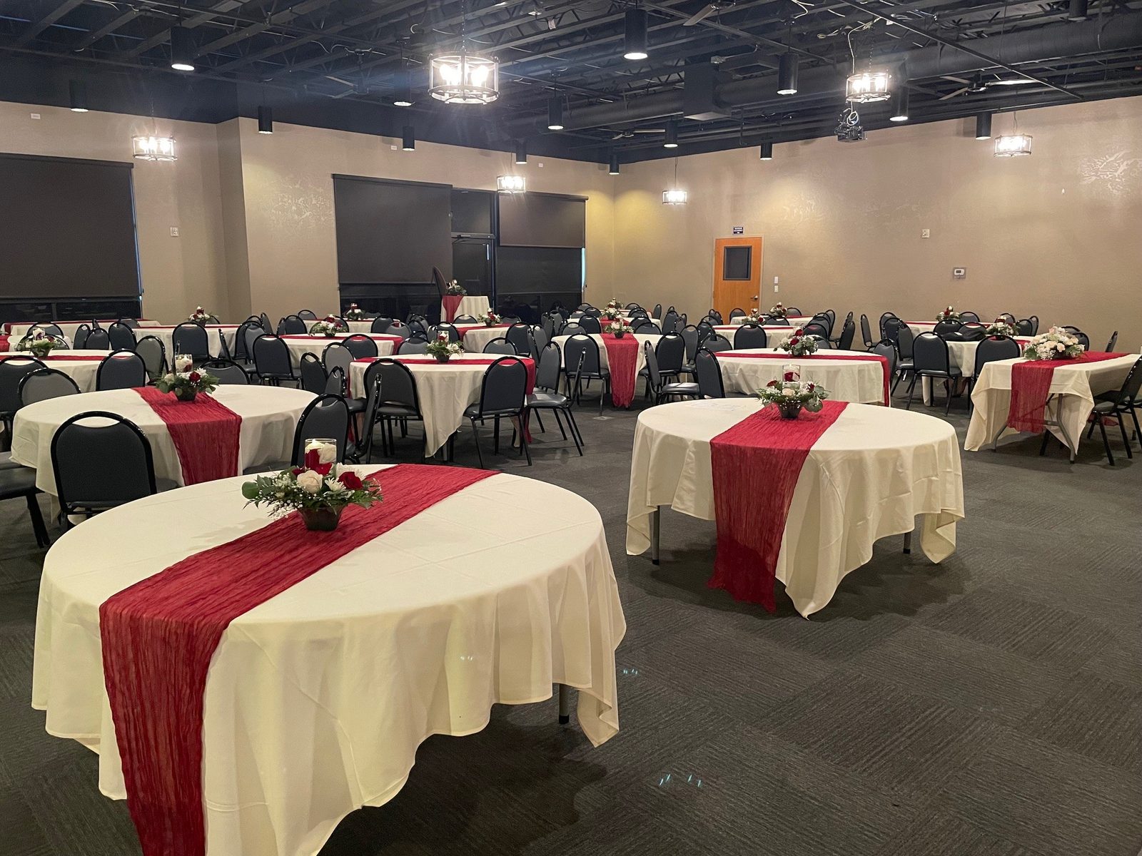 A reception set with round tables, ivory linens, red runners, and floral centerpieces in the CG Event Center