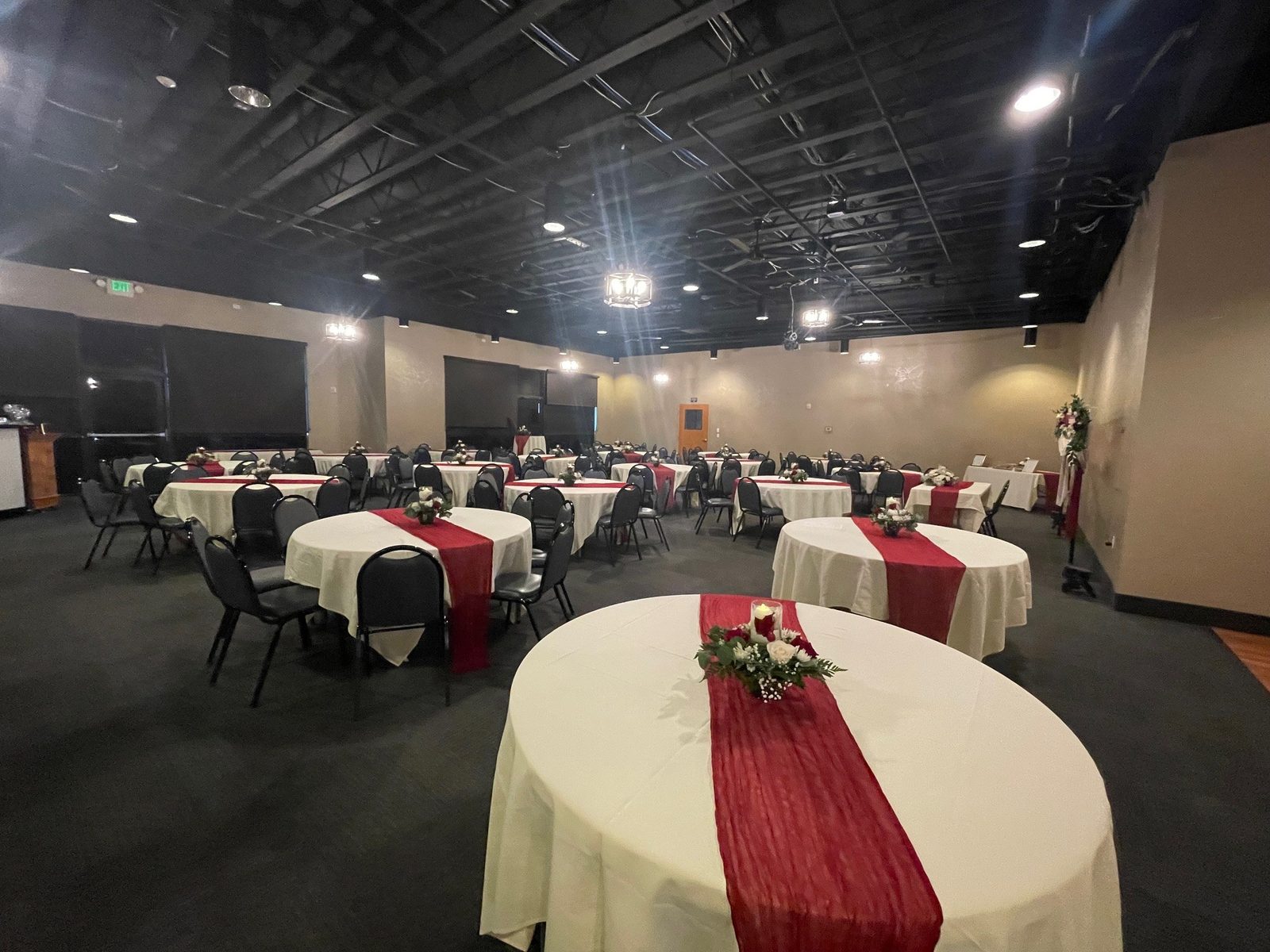 Round tables with red runners and floral centerpieces in the CG Event Center banquet hall at CG Public House