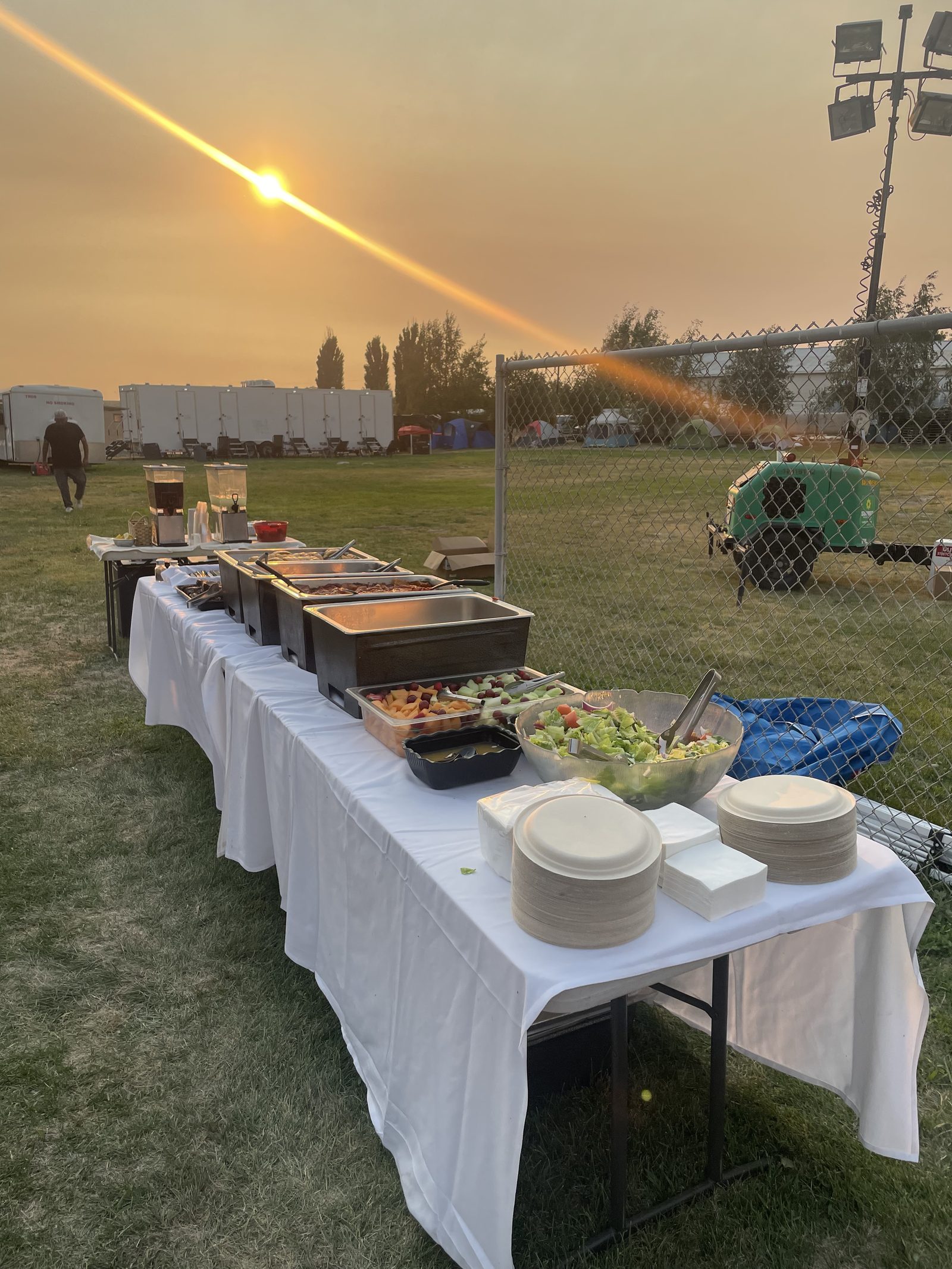 A CG Public House & Catering buffet spread with chafing dishes and fresh salad set up at the Lyons Ferry Fire base camp near Kahlotus, Washington, at sunset