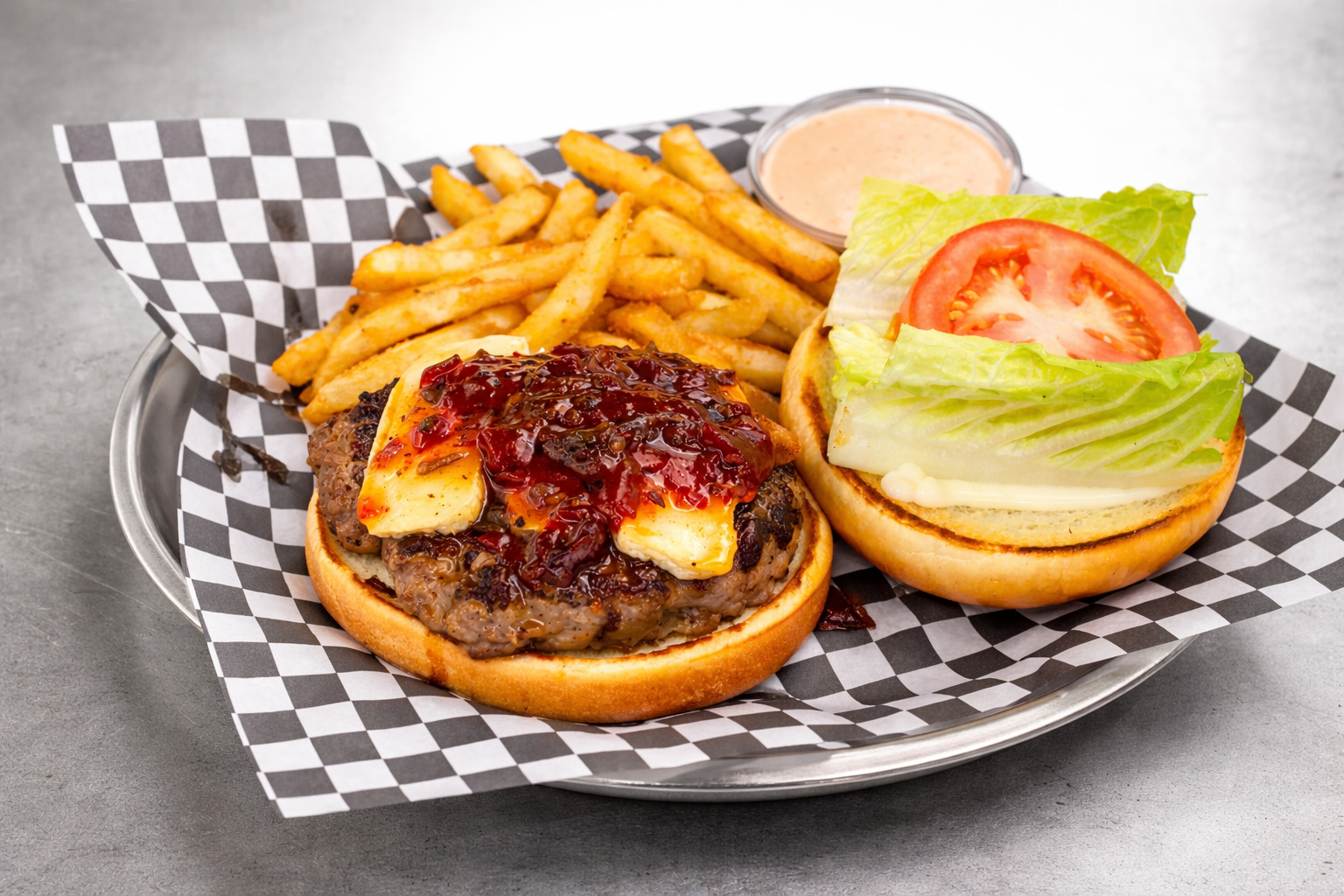 Burger topped with brie and bacon jam, with lettuce, tomato, fries and dipping sauce