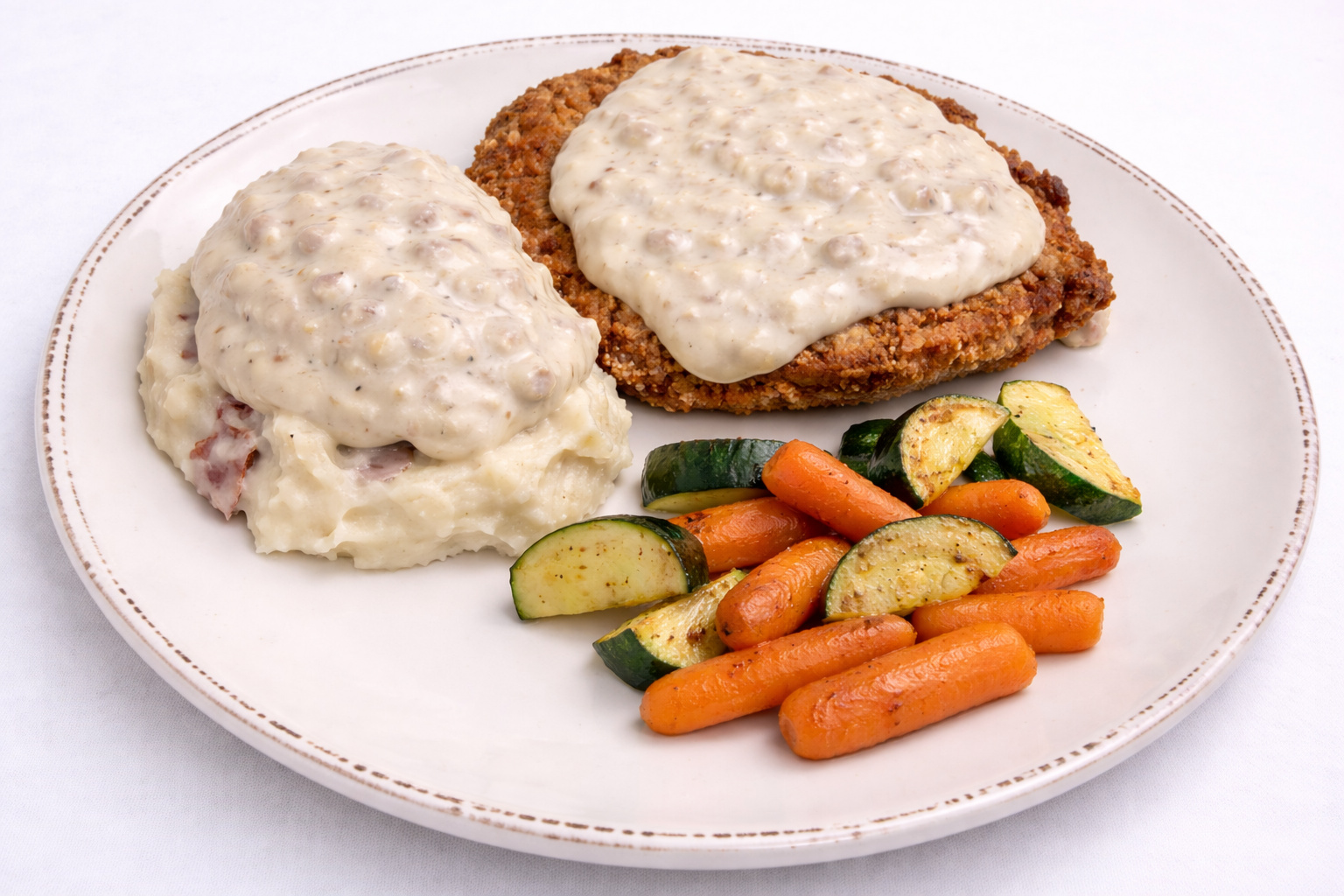 Chicken fried steak with country gravy over mashed potatoes and roasted zucchini and carrots