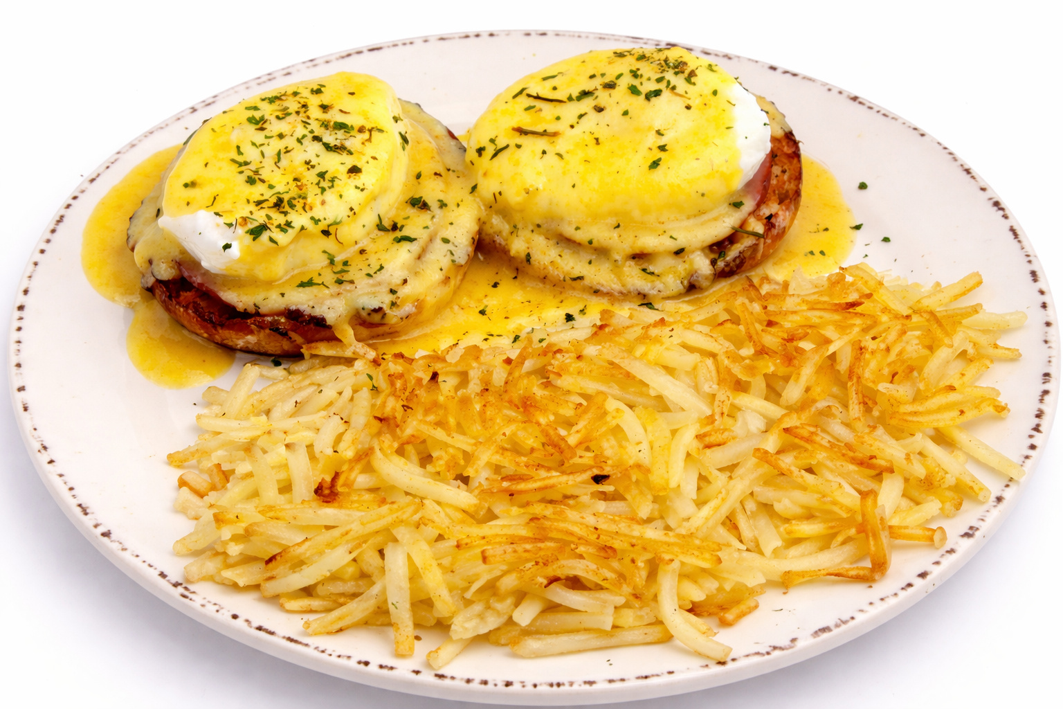 Eggs Benedict topped with hollandaise sauce, served with hash browns